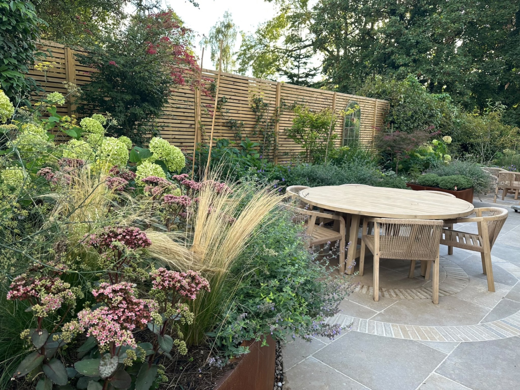 The circular timber dining terrace surrounded by layered planting and a slatted timber screen in the Hambledon garden